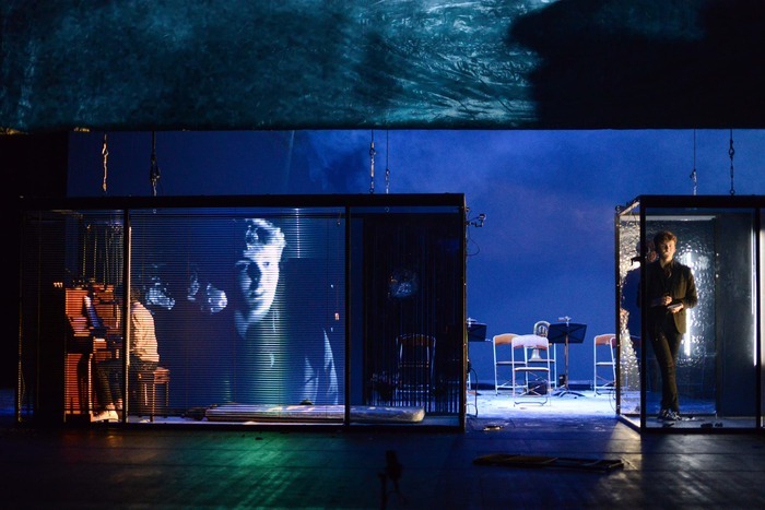 Un plateau de théâtre avec de la vidéo, deux comédiens et un instrument de musique.