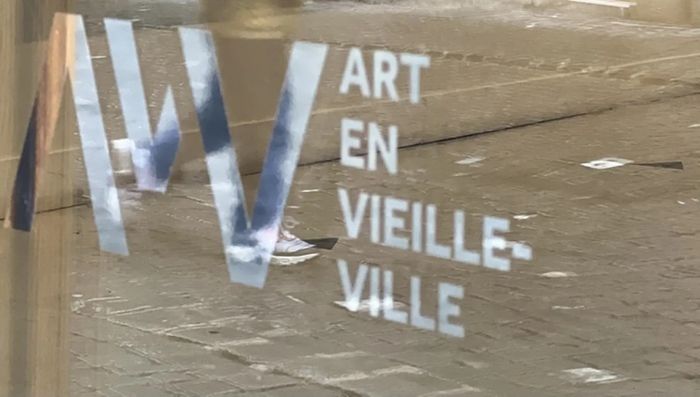 logo AVV sur une vitrine dans laquelle se reflète un enfant qui marche