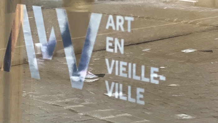 logo AVV sur une vitrine dans laquelle se reflète un enfant qui marche