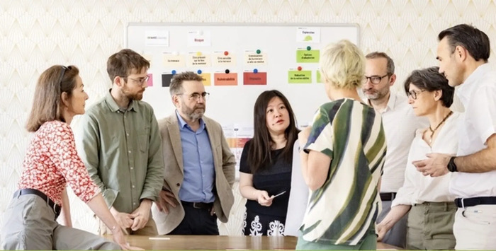 AdACC Une équipe composée d' hommes et de femmes discutent avec des cartes en main devant un mur avec la méthodologie pour développer des solutions d' adaptation au changement climatique.