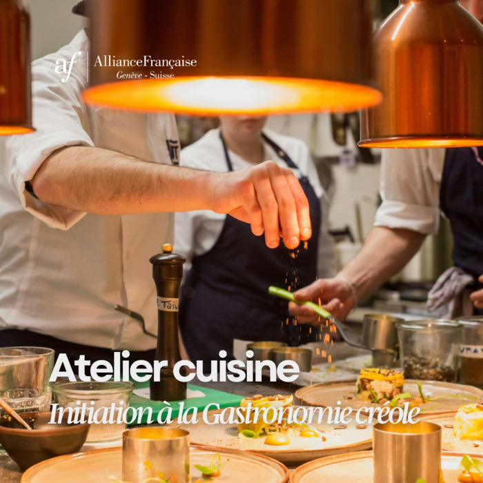 Photographie en gros plan dans une cuisine professionnelle montrant un chef de profil, en veste blanche, qui saupoudre d'épices une assiette soigneusement dressée. En arrière-plan, d'autres cuisiniers en tablier bleu s'activent sous des lampes chauffantes en cuivre. En haut à gauche figure le logo blanc de l'Alliance Française Genève - Suisse. En bas, le texte en blanc indique : "Atelier cuisine - Initiation à la Gastronomie créole".