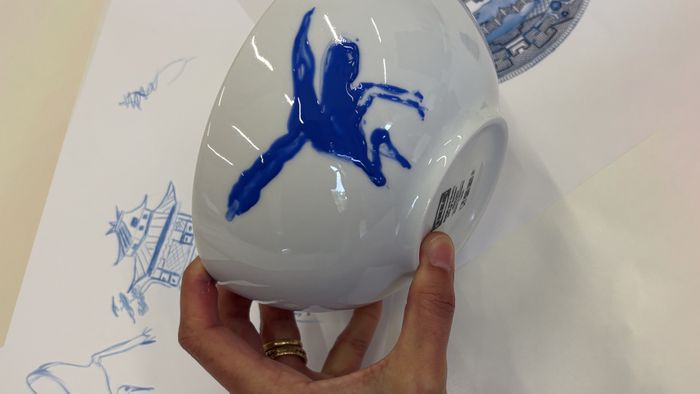 Une personne est en train de dessiner un décor bleu sur une porcelaine.