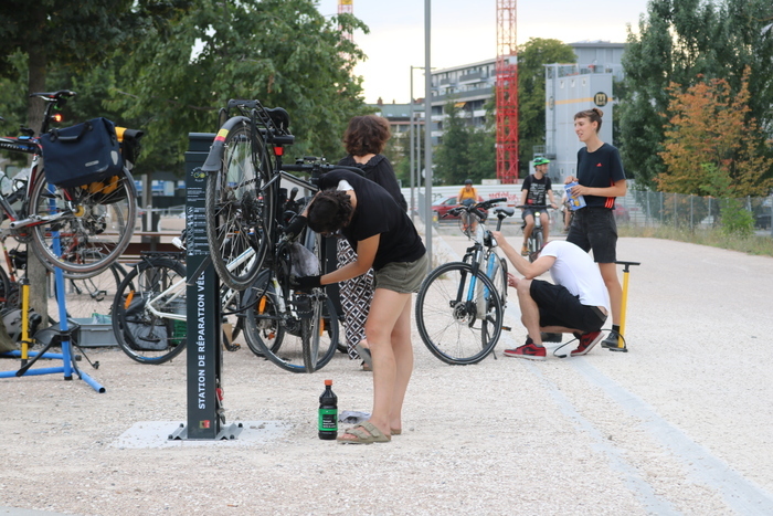 Plusieurs personnes discutant et réparant leur vélo à la borne d'auto-réparation de la voie verte