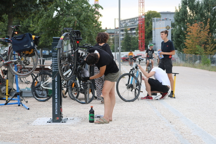 Plusieurs personnes discutant et réparant leur vélo à la borne d'auto-réparation de la voie verte