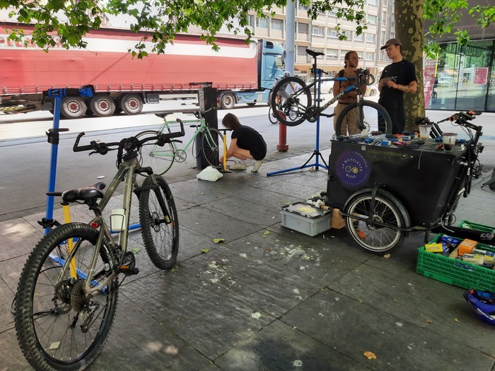 Plusieurs personnes discutant et réparant leur vélo à la borne d'auto-réparation du parvis d'Uni Mail