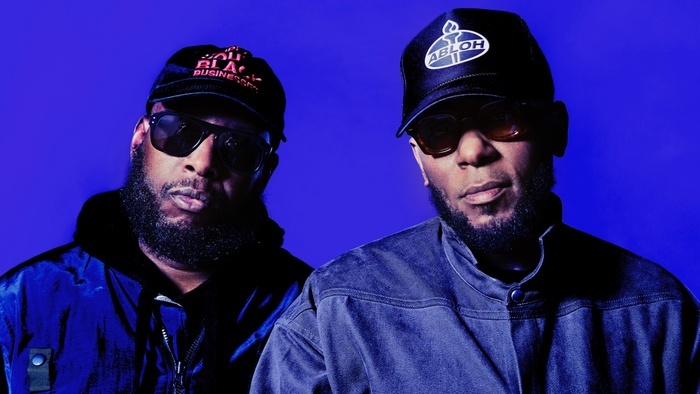 Photo de Talib Kweli et Yasiin Bey qui portent casquettes et lunettes de soleil