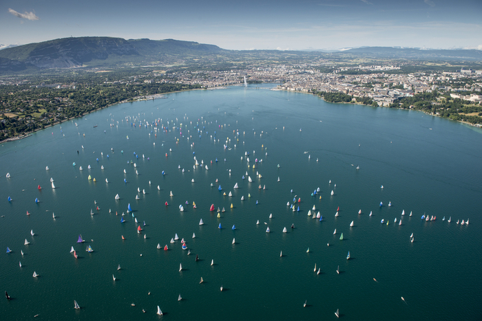 DR Sur cette image, on aperçoit une partie du lac Léman avec, au fond, la ville de Genève. On distingue également le jet d'eau et les montagnes qui entourent la ville. De nombreux bateaux à voile parsèment le lac, ajoutant une touche dynamique à ce paysage pittoresque.
