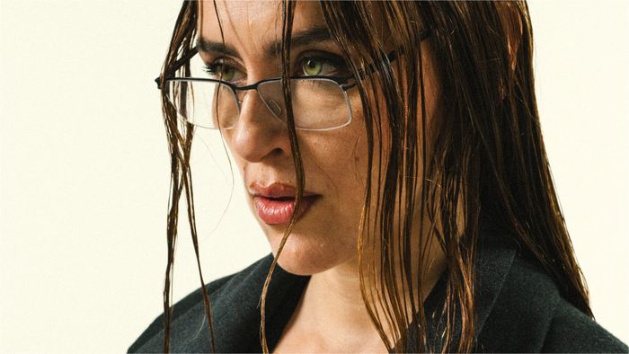 Une femme est en gros plan, elle porte des lunettes et a les cheveux longs foncés.