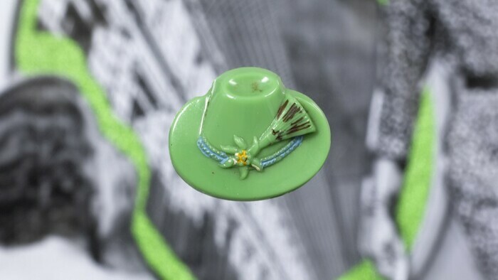 Un bouton vert pomme en forme de chapeau est disposé sur une image en noir et blanc et légèrement floue représentant des femmes