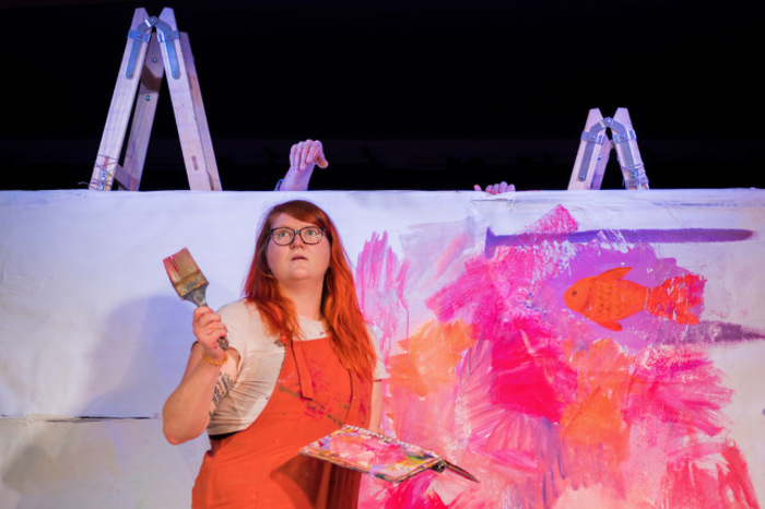 Une jeune femme avec un gros pinceau à la main devant une grande peinture