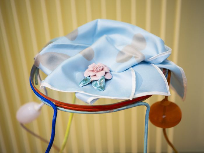 Broche en céramique réalisées par Marie Ducaté. Elle a la forme d'une fleur et est posée sur un foulard de couleur bleu.