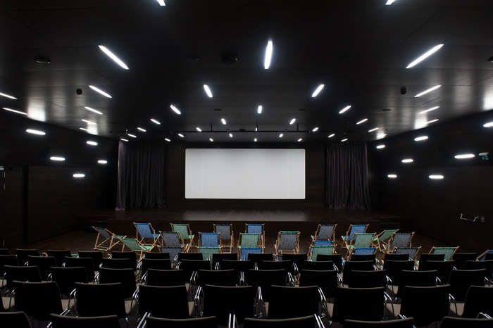 Salle de cinéma du MEG - auditorium avec un grand écran et devant des transats et des chaises.