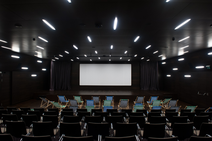Salle de cinéma du MEG - auditorium avec un grand écran et devant des transats et des chaises.