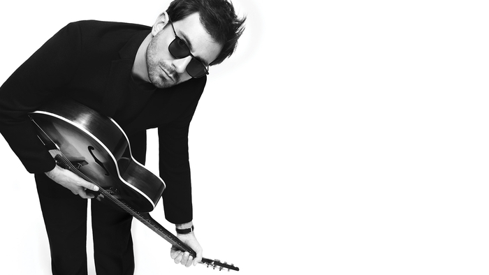 Photo du chanteur de Cocoon qui joue de la guitare acoustique et porte des lunettes de soleil