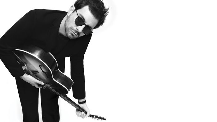 Photo du chanteur de Cocoon qui joue de la guitare acoustique et porte des lunettes de soleil