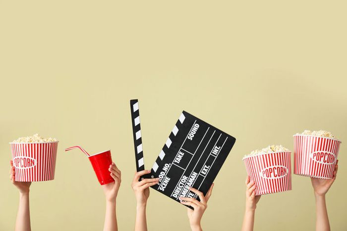 Une photo en couleur avec des mains qui portent des contenants de pop-corn et un clap de cinéma.
