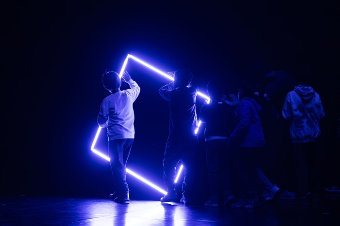 © Des enfants en mouvement devant un carré fait de neon bleu