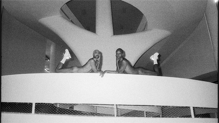 Deux hommes posent nus avec des baskets blanches allongés sur un escalier.