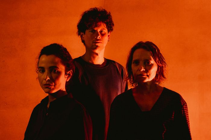 Portrait de trois comédien.nes sous une lumière rouge.