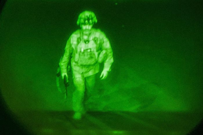 Photographie en vue nocturne en tons de vert montrant un soldat américain marchant avec un fusil à la main en direction de la camera.