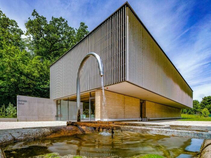 Bâtiment moderne de la Maison du Futur à Vessy, avec fontaine au premier plan et arbres en arrière-plan.