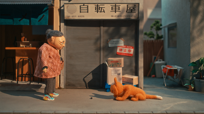 Sur un trottoir, une figurine de femme âgée asiatique en face d'une figurine de chat roux.