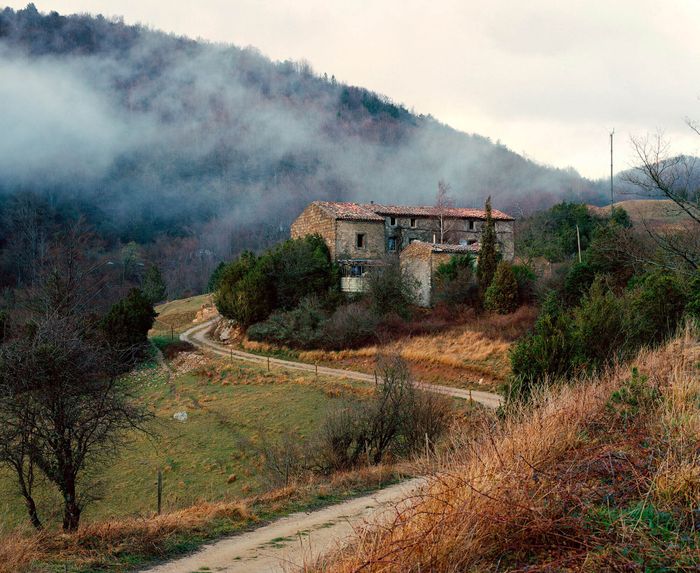 Photo d'une vieille maison sur une colline, avec une route qui y mène et de la brume