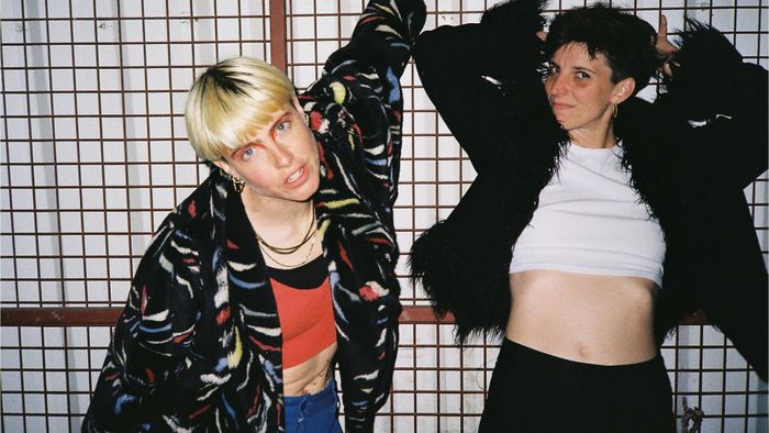 Deux femmes posent devant un grillage.