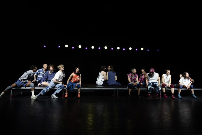 Sur cette image, il y a douze comédiens et comédiennes assis et séparés en trois groupes, il y sur les extrémités 2 groupes de 5 comédiens et un groupe de deux comédiens au centre de l'image. Chacun des comédiens à une expression de visage différente.