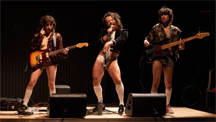 Trois personnes jouent de la guitare sur scène avec des vestes en cuir.