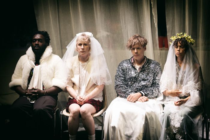Quatre personnes en habits de mariage, assistantes ou ayant assisté à une cérémonie, sont assises sur des chaises, leurs visages exprimant une austérité profonde.
