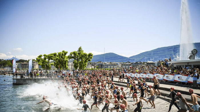 Cette image montre le départ impressionnant du Triathlon de Genève.
On voit une foule d'athlètes se jeter dans le lac Léman.