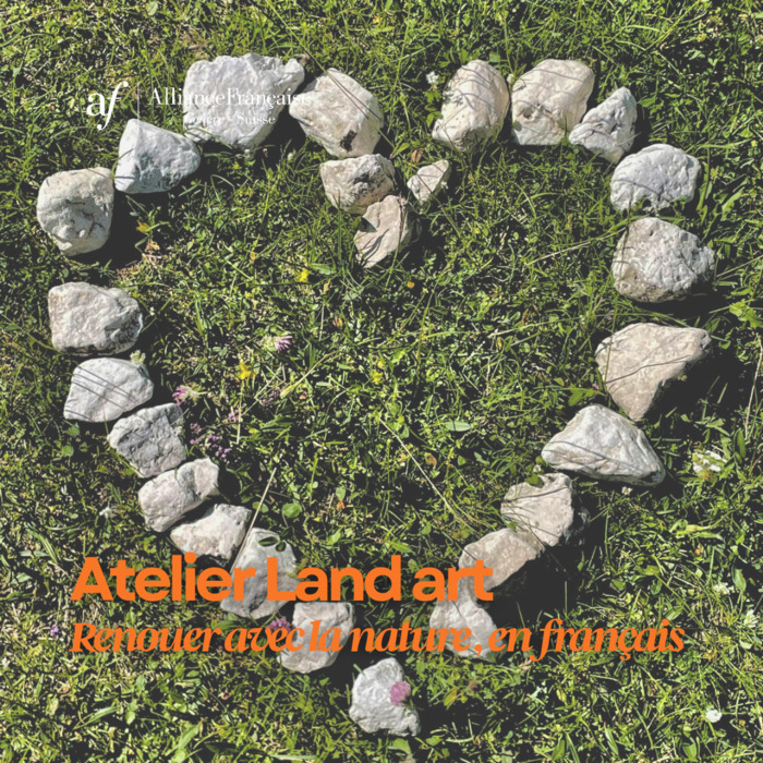 Photographie en vue aérienne montrant un grand cœur dessiné sur de l'herbe verte et fleurie à l'aide de galets blancs et gris. En haut à gauche, le logo blanc de l'Alliance Française Genève - Suisse est visible. En bas, le texte superposé en orange indique : "Atelier Land art - Renouer avec la nature, en français".