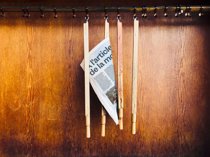 Une photo de quatre baguettes de journaux suspendus à des crochets, dont une avec un journal sur lequel on devine le titre du spectacle.