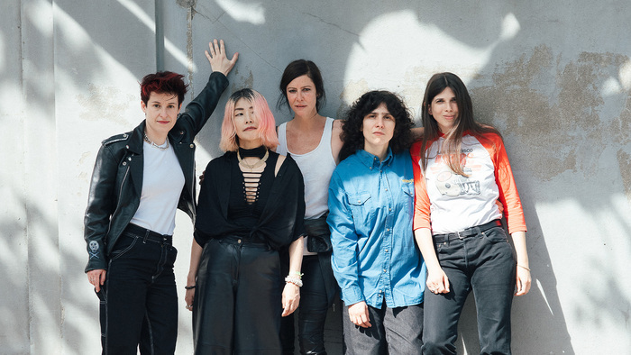Photo des 5 membres du groupe qui posent debout devant un mur