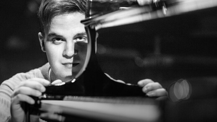 Portrait en noir et blanc de l'artiste qui se tient à hauteur du clavier de son piano