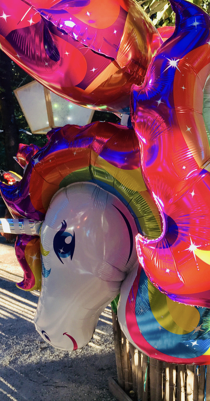 Un tas de balons colorés, on voit en premier plan une licorne sur les tons fucsia et arc en ciel.