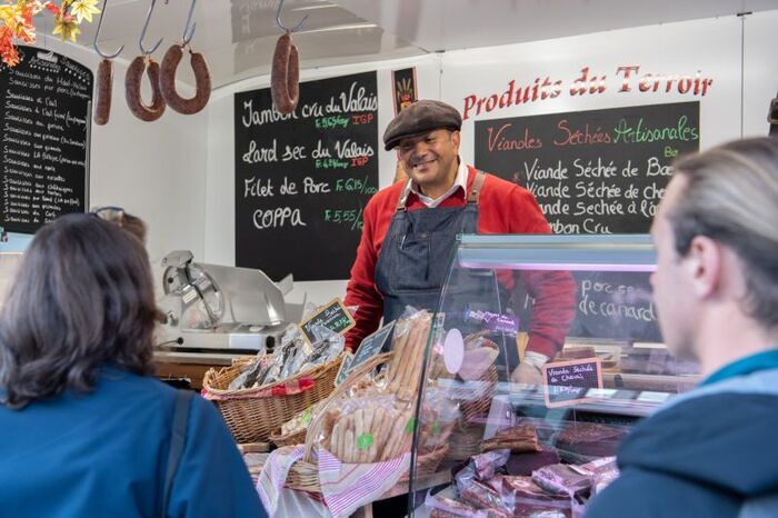 Nous voyons un marchand servir du fromage et de la charcuterie valaisanne dans son food truck à des clients