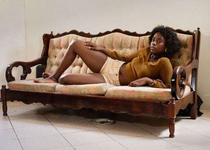 Jeune femme noire allongée sur un vieux divan, regardant l'objectif