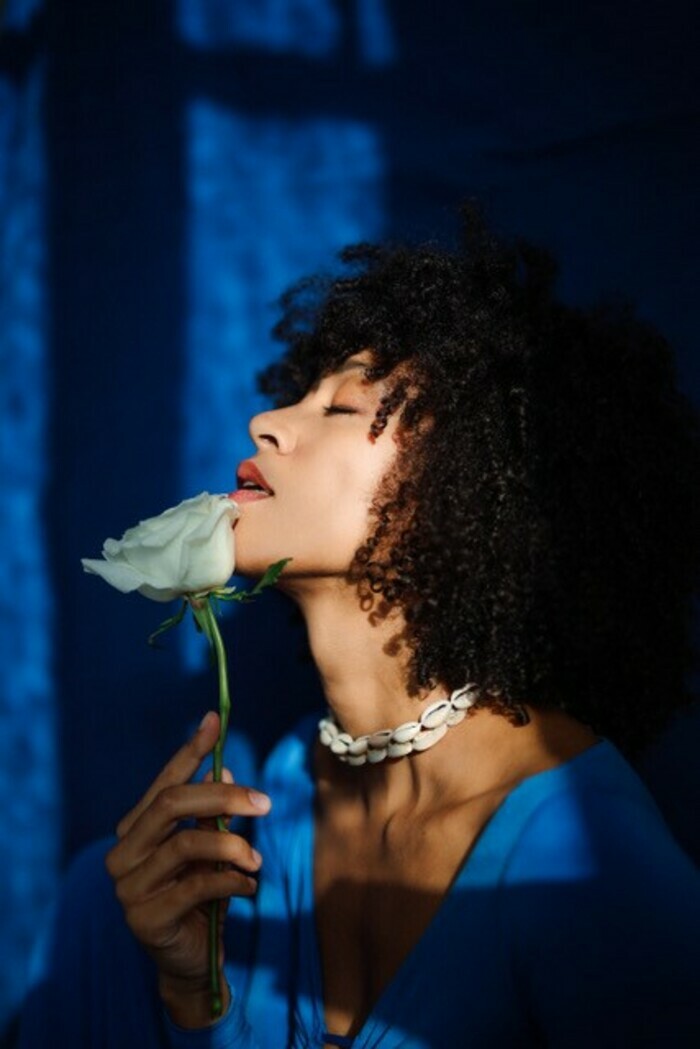 Femme afro tenant une rose blanche dans un rayon de lumière