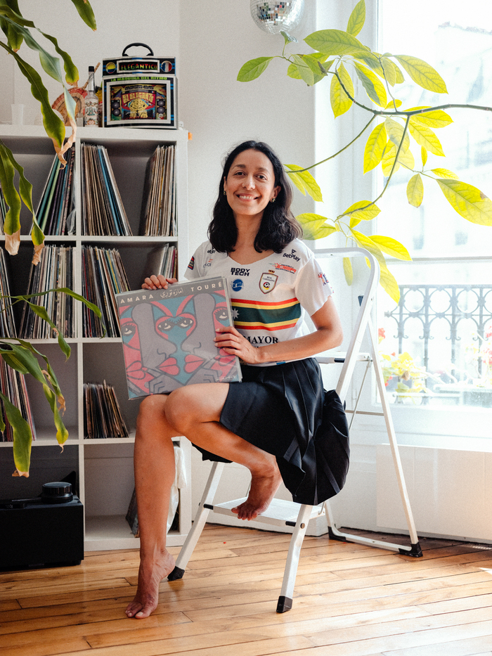 Une femme adulte souriante assise et tenant une pochette vinyle coloré tout en regardant la caméra