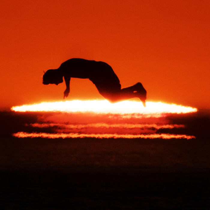 Photo contemporaine d’un coucher de soleil avec la silhouette d’un homme sautant parallèlement au soleil dans la pénombre.