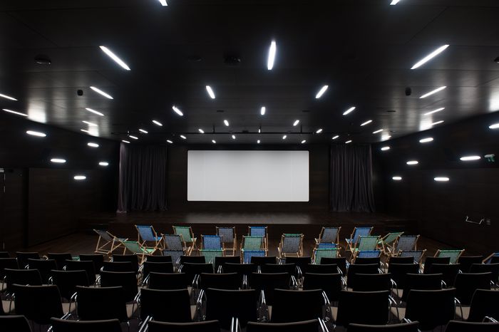 Salle de cinéma du MEG - auditorium avec un grand écran et devant des transats et des chaises.