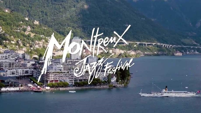 L'image montre une vue aérienne en plongée de la ville de Montreux, un grand bateau à vapeur traditionnel blanc.