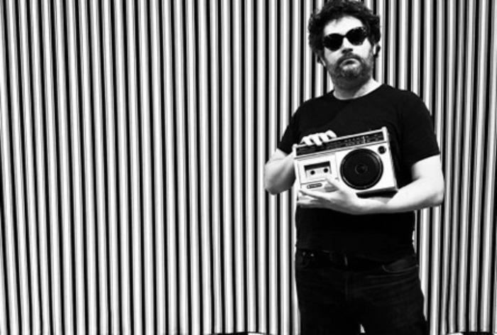 Une photo en noir et blanc : fond rayé et Mr Hobbs avec des lunettes noires et un lecteur de cassettes des années 80.