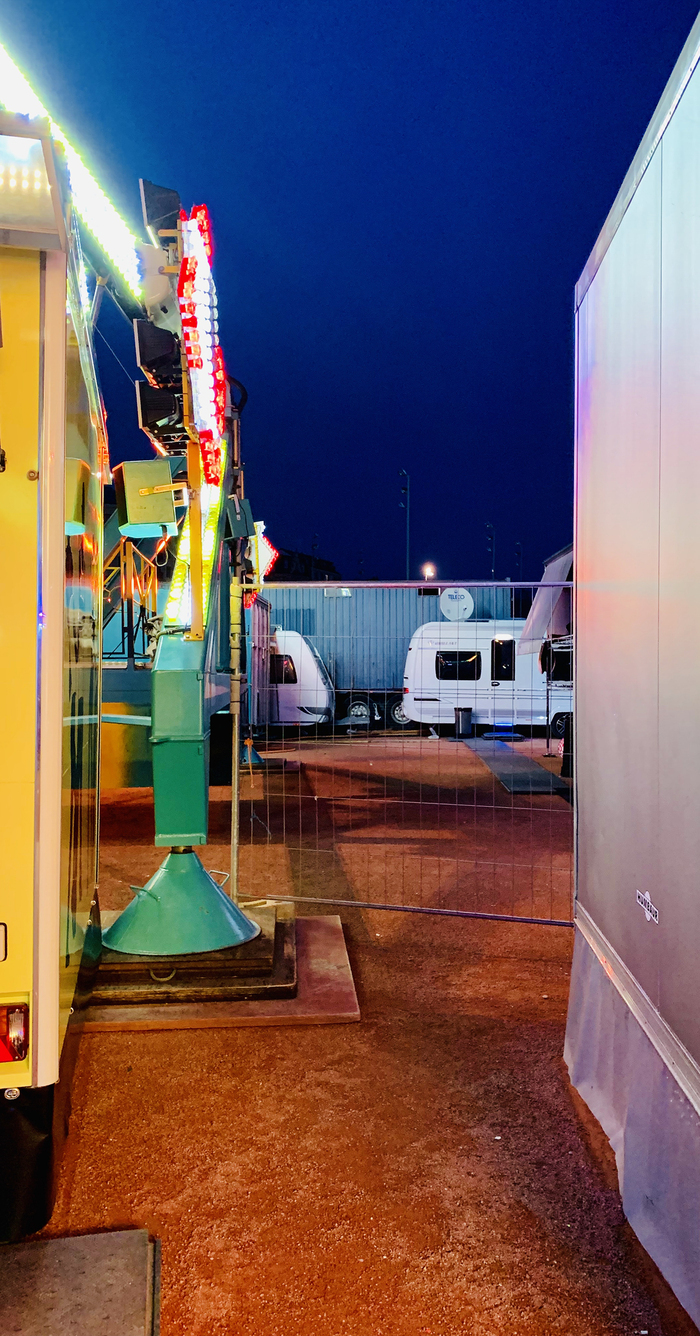 © Magali Dougados C'est une photo d'une allée d'un parc d'attraction. On aperçoit des roulottes au loin et à gauche des lumieres colorées typique d'un manège.