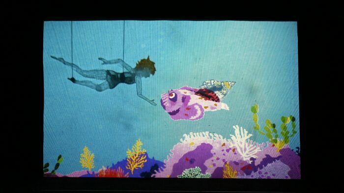 Océan (c) Succursale 101 La figurine d'une fille en marionnette à tiges suit un coquillage au fond de l'océan au dessus d'un banc de corail coloré.