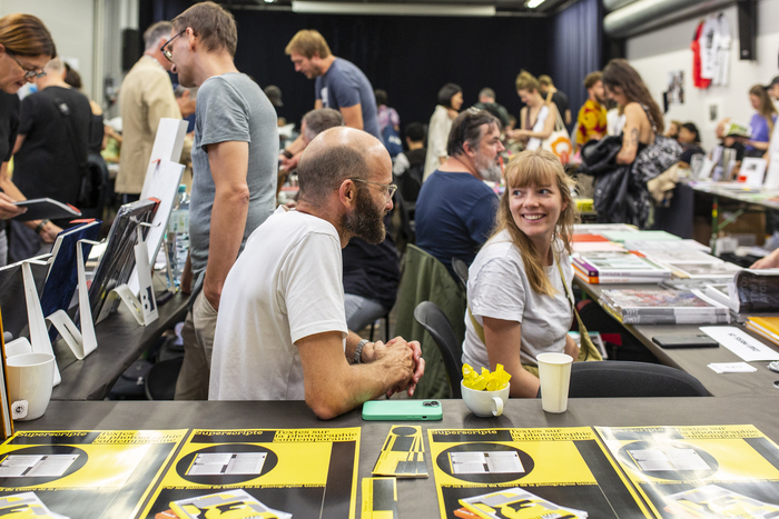 Aline Bovard Rudaz Photographie de la foire du livre photographique où les livres sont présentés sur des tables, entourés des éditeurs et des visiteurs qui les regardent et les feuillettent.