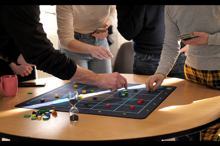 Joueurs autour d'un plateau de jeu avec leurs téléphones et un sablier