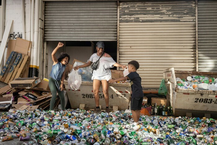 A melhor mãe do mundo
Anna Muylaert Une mère et ses enfants sautent en souriant dans un tas de déchets (des canettes vides)